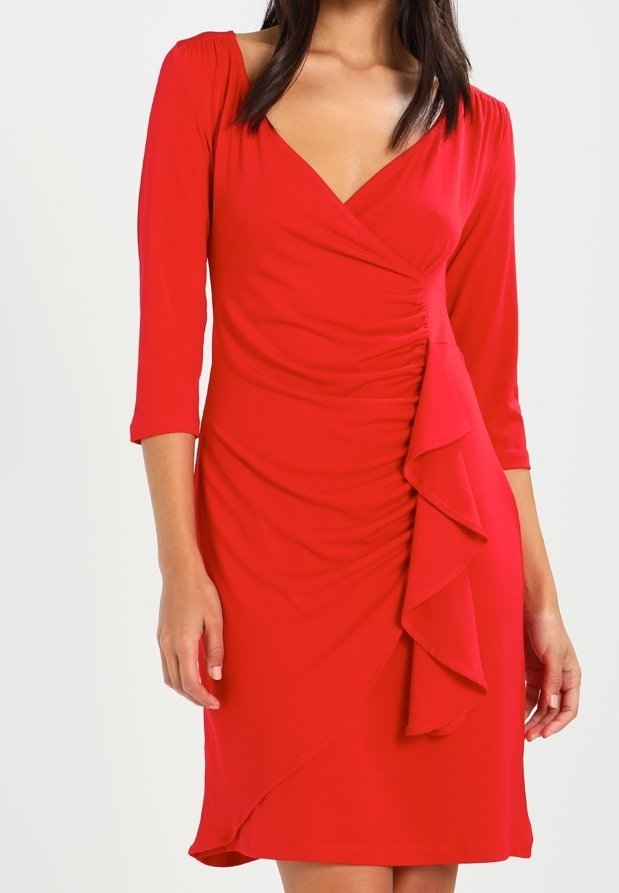 Femme portant une robe rouge longueur genou avec des manches trois-quarts, un col en V, une taille froncée et un volants en cascade à l'avant.