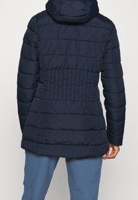 Manteau matelassé bleu marine avec un design matelassé, une capuche et une taille cintrée. Texture lisse avec des coutures horizontales et un bas légèrement évasé.