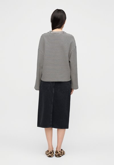 Μπλούζα με μαύρες και λευκές ρίγες σε χαλαρή γραμμή, συνδυασμένη με μαύρη μίντι φούστα από τζιν και παντόφλες με λεοπάρ σχέδιο.