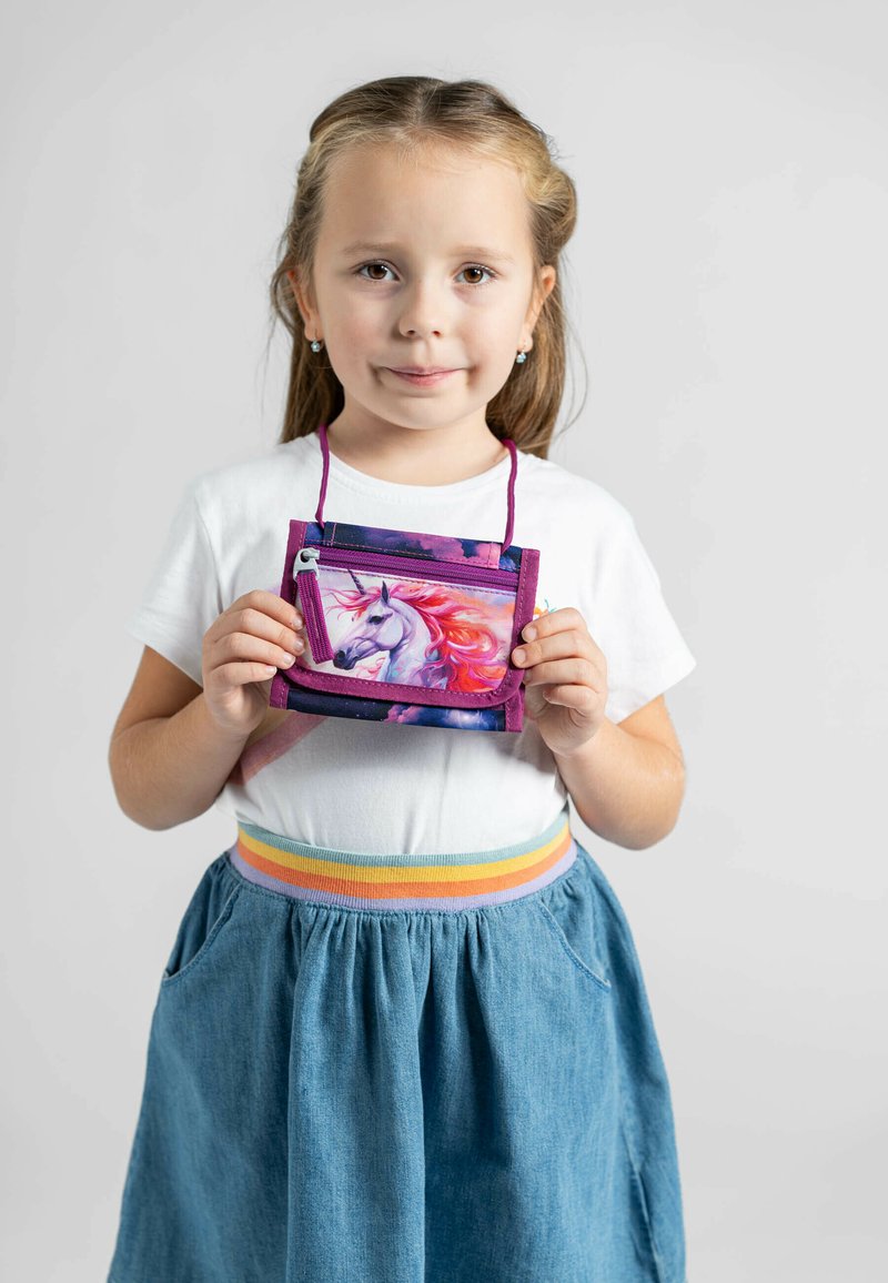 Portafoglio compatto viola con un grafico di unicorno, dotato di un scomparto con zip e una tracolla. Il modello indossa una camicia bianca e una gonna di jeans.