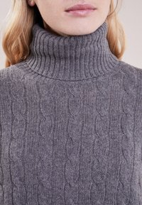 Suéter de punto gris con cuello alto acanalado, patrones de trenzado texturizado y una suave mezcla de lana, que proporciona calidez y comodidad.