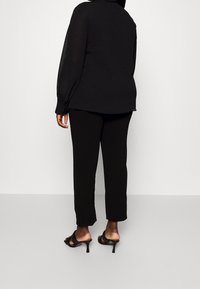 Svart långärmad blus med lös passform, parat med svarta tapered byxor och högklackade sandaler. Slät tyg och minimalistisk design.