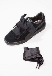 Baskets en daim noir avec lacets larges en ruban satin noués en nœud, accompagnées d'une paire supplémentaire de lacets en satin noir sur fond blanc.