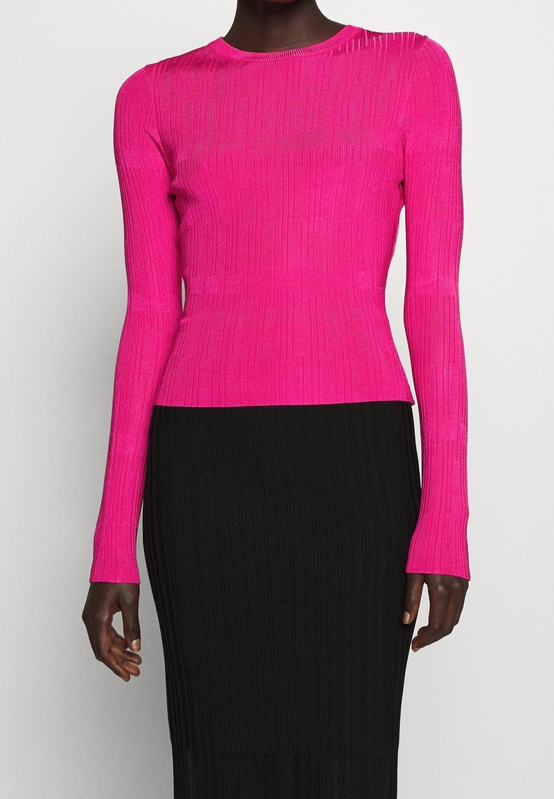 Top aderente a maniche lunghe in tessuto rigato rosa brillante, con scollatura rotonda e cuciture accentuate, abbinato a una gonna nera con texture.