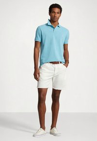 Ανοιχτό μπλε πόλο μπλουζάκι από αεριζόμενο ύφασμα, σε συνδυασμό με λευκά τζιν σορτς με ξεφτισμένα τελειώματα. Καθημερινά λευκά πάνινα παπούτσια.