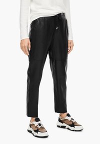 Pantalons de jogging en cuir noir avec une taille élastique et un cordon de serrage, accompagnés de baskets chunky avec des accents marron, noir et blanc.