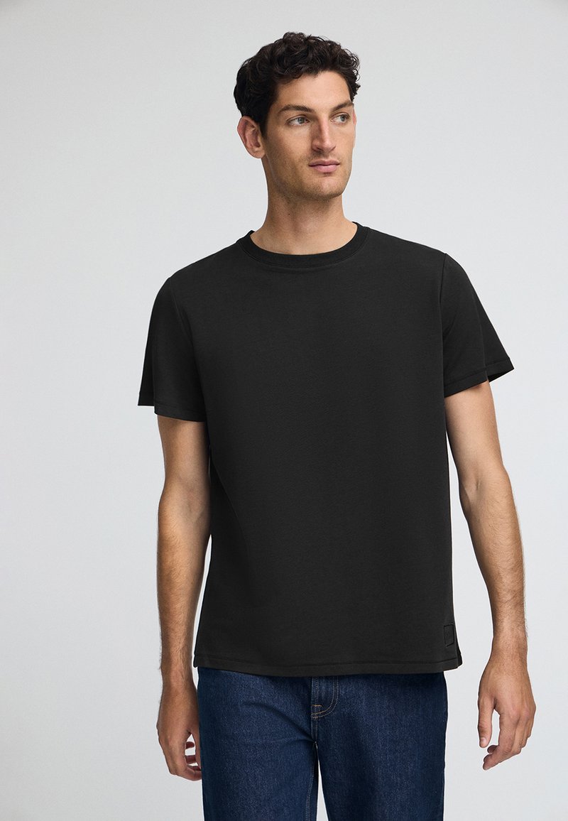 Zwarte katoenen T-shirt met een ronde hals, korte mouwen en een rechte snit. Opvallende details zijn een klein etiket aan de zoom.