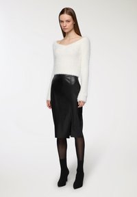 Pullover bianco croppato peloso con maniche lunghe, abbinato a una gonna midi in pelle nera con spacco frontale, collant neri trasparenti e stivaletti neri.