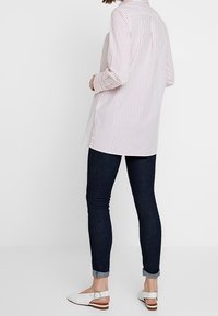 Chemise à rayures boutonnée en rose clair et blanc, avec manches longues et empiècement au dos, associée à un jean slim foncé et des ballerines blanches.
