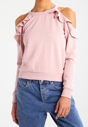Růžové dlouhý rukáv top s odhalenými rameny a volánkovými detaily na ramenou, ve spojení s modrými džínami s vysokým pasem.