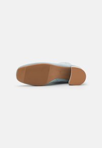 Chaussure slip-on bleu clair avec un dessus texturé, un bout arrondi et une semelle en caoutchouc flexible présentant un accent lisse, tan, au niveau du talon.