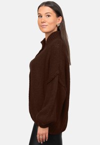 Pull-over en tricot marron avec un col montant et des manches surdimensionnées. Tissu texturé avec une coupe décontractée, agrémenté de détails côtelés.