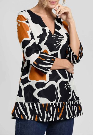 Donna che indossa una blusa a motivo floreale astratto nei colori nero, bianco e arancione con scollo a V e maniche a tre quarti, abbinata a jeans blu scuro.