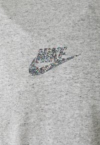 Pelēks sporta krekls ar mirdzošu, daudzkrāsainu mirdzoša Nike logo uz priekšpuses. Materiāls ir mīksts, ar teksturētu apdari un kripatiņām.