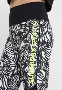 Leggings a motivi bianco e nero con vita alta e il logo "SUPERDRY" giallo brillante lungo il lato. Tessuto liscio e elasticizzato.