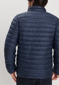 Giacca puffer blu navy con motivo a zig zag orizzontale, colletto alto e polsini elasticizzati. Realizzata in materiale lucido e leggero.