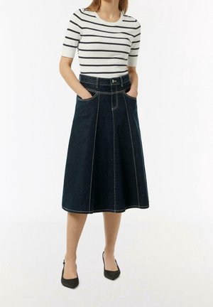 Jupe en denim foncé en ligne A avec des coutures claires, dotée d'une taille haute, de deux poches latérales et d'un ourlet au genou. Associée à un top rayé.