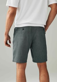 Shorts gris texturé avec deux poches arrière, portés avec une chemise blanche à manches courtes. Présente une taille élastique pour un confort optimal et une coupe décontractée.