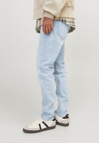  Lichtblauwe denim jeans met een slim fit, met een lichte scheur op de knie. Gecombineerd met crèmekleurige en zwarte sneakers.