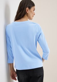 Lichtblauw geribbelde langemouwen top met een brede ronde halslijn en driekwartmouwen, gecombineerd met zwarte broek.