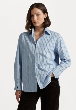 Camisa de botão azul-claro com riscas brancas verticais, corte ajustado, mangas longas e um pequeno logótipo na barra da manga. Tecido de algodão texturizado.