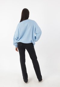 Lichtblauwe gebreide trui met een relaxte pasvorm en geribbelde textuur, gecombineerd met zwarte flared jeans, van achteren afgebeeld tegen een witte achtergrond.