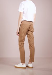 Tan chinos made of cotton, featuring a slim fit and rolled cuffs. Paired with a plain white t-shirt and white sneakers with a gum sole.