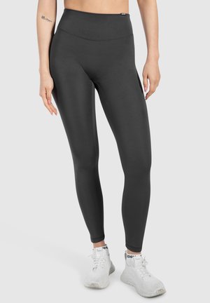 Hoge taille zwarte legging met een gladde, rekbare textuur, een getailleerd ontwerp en verstevigde stiksels. Draagt met witte sportschoenen.