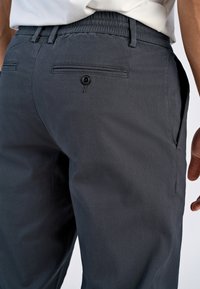 Chinos gris foncé à coupe décontractée, avec une jambe fuselée, des poches arrière avec fermeture à bouton et une taille élastique pour plus de confort.