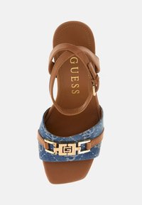 Brown synthetic leather heel with a denim strap featuring a gold buckle and logo accent. Square toe with a flat sole.