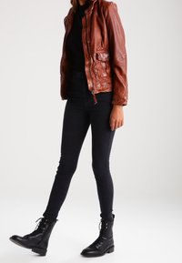 Brun läderjacka med dragkedja framtill, två sidofickor, i kombination med svarta slim-fit jeans och svarta snörade kängor. Slät textur, karvdesign.