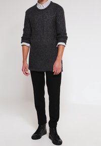 Pull en maille gris foncé à col rond, associé à une chemise à col bleu clair. Porté avec un pantalon noir et des chaussures à lacets noires.