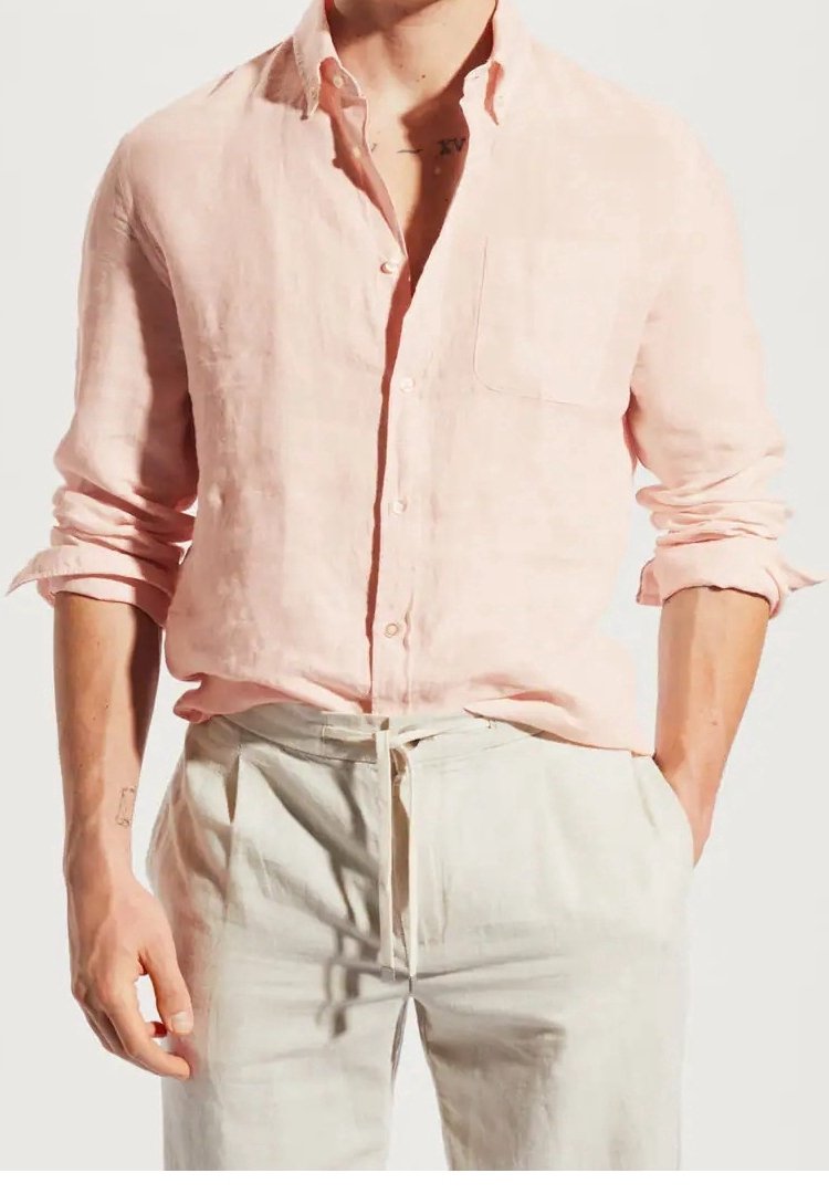 Homme portant une chemise rose clair à manches longues avec manches retroussées et un pantalon beige clair à taille cordon.