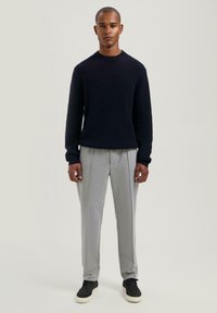 Marineblauwe ribgebreide trui, grijze geplooide broek en zwarte sneakers. De outfit heeft een relaxed fit en een gestructureerd materiaal.