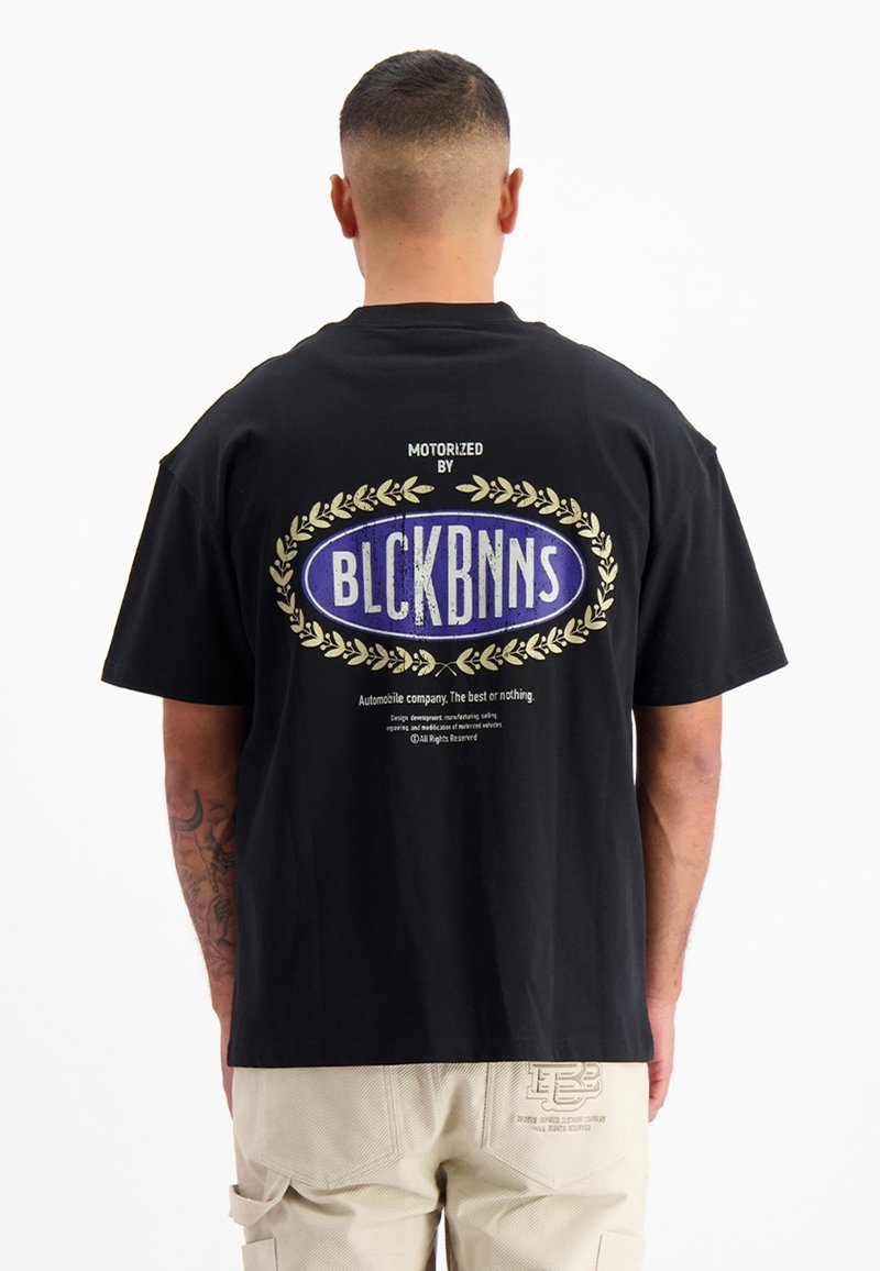 Zwarte katoen t-shirt met een grote paarse en witte grafiek op de achterkant, met lauweraccenten en tekst, gecombineerd met beige cargo shorts.