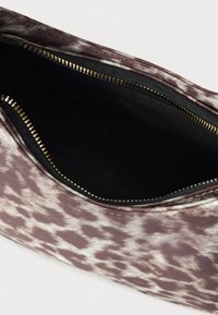 Posnetek iz bližine roza-bele torbice z vzorcem, z zadrgo z zlatimi zobci in črto notranjega podstavka iz črnega blaga.