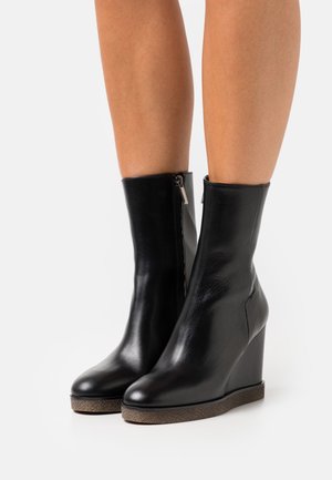 Black leather wedge ankle boots with a smooth texture, side zipper, and a contrasting textured sole. Sleek and fitted design.