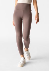 Leggings marroni a vita alta in un tessuto liscio e elastico, abbinati a sneaker bianche. Il design presenta una silhouette aderente.