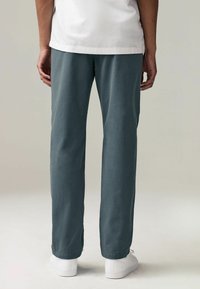 Pantaloni tapered da uomo in morbido tessuto testurizzato, di colore blu polveroso, con una vestibilità comoda, abbinati a sneaker bianche.