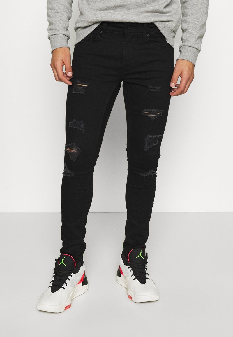 Jeans skinny negros rasgados con detalles de desgaste, combinados con zapatillas blancas y negras con acentos rojos y verdes.