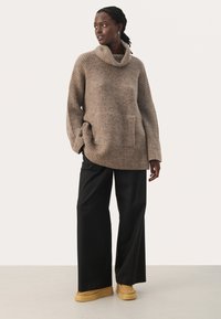Beige Übergröße-Pullover mit einem Kragen und geripptem Muster, kombiniert mit schwarzen weit geschnittenen Hosen und beige Slippern.