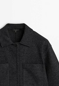 Dunkelgraue Wolljacke mit Kragen, ausgestattet mit zwei Fronttaschen und einer Knopfleiste. Weiche Textur, strukturierter Schnitt und taillierte Passform.