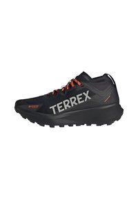 Chaussure de trail running noire avec une tige en GORE-TEX, accents orange, marque TERREX bien visible, semelle texturée et un design élégant et léger.