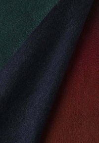 Trois pièces de feutre en laine dans des teintes de vert foncé, bleu marine et brun rougeâtre, mettant en valeur une texture douce et une épaisseur uniforme.