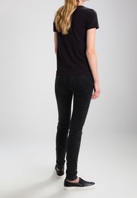 Camiseta negra combinada con jeans negros texturizados y zapatos slip-on negros. El conjunto presenta un diseño sencillo sin patrones ni herrajes visibles.