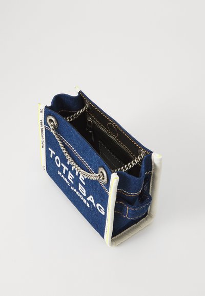 Geantă din denim cu mânere din lanț, imprimeu alb cu logo și cusături contrastante. Parte superioară deschisă, interior cu buzunar cu fermoar și colțuri întărite.