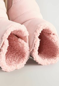 Rozā zābaki ar mīkstu, teksturētu oderi un gludu ārpusi. Iezīmējas ar pūkainu dizainu un šuvju detaļām ap malām.