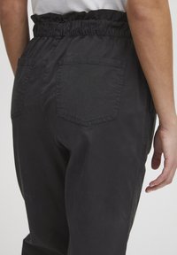 Pantalon en mélange de coton noir avec une taille élastique, doté de deux poches arrière, d'une coupe décontractée et de détails de couture visibles.