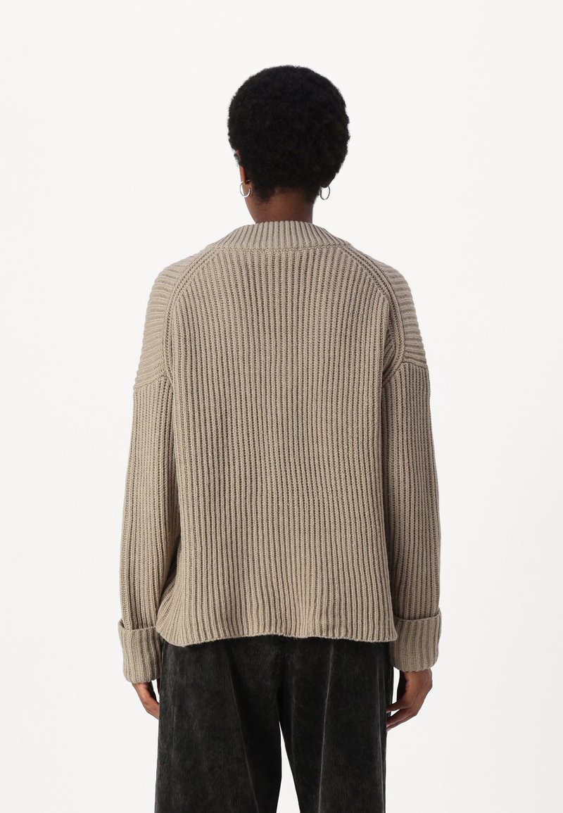 Beiger Rippstrickpullover mit rundem Halsausschnitt und umgeschlagenen Bündchen, in lockerer Passform und mit strukturiertem Stoff, kombiniert mit dunklen, lockeren Hosen.