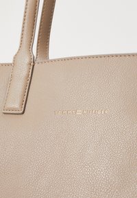 Sac fourre-tout en cuir texturé beige au design épuré. Présente un logo doré "TOMMY HILFIGER" et des anses robustes.